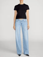 Person wearing light blue jeans and a black top on a plain background