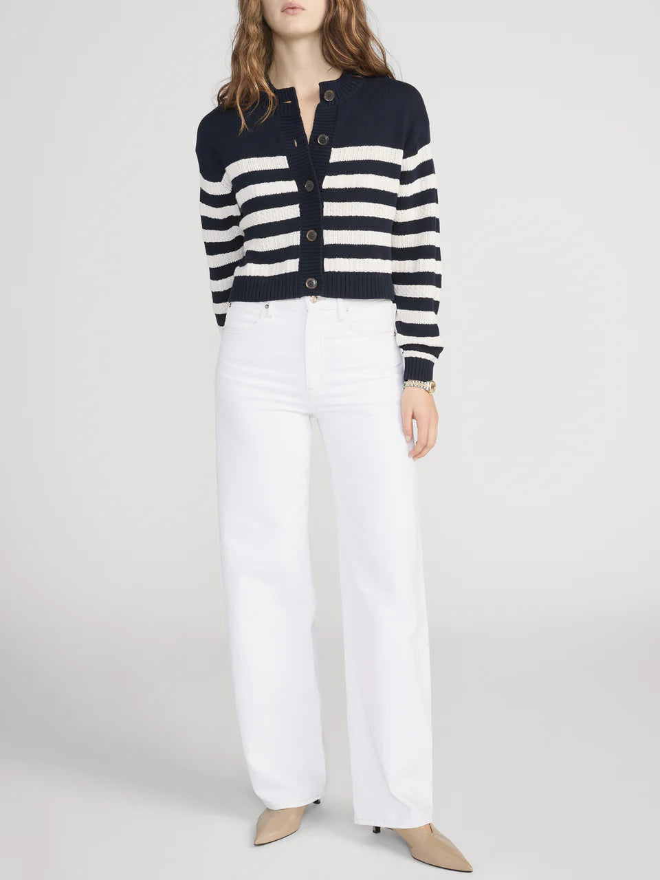 Person wearing a navy and white striped cardigan with white pants on a light gray background