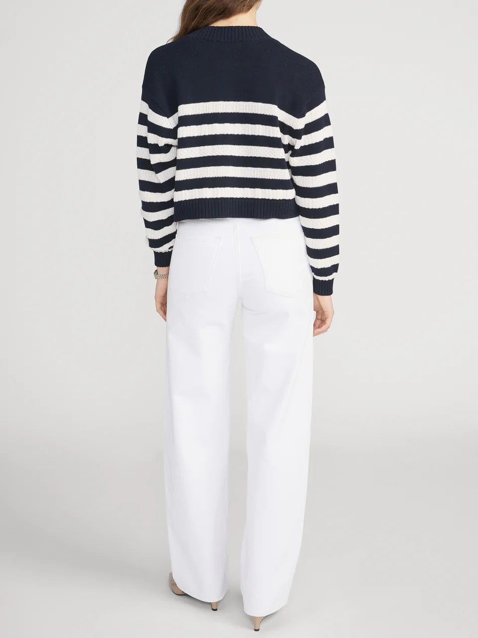Person wearing a navy and white striped sweater with white pants on a light gray background