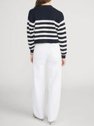 Person wearing a navy and white striped sweater with white pants on a light gray background