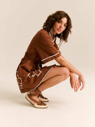 Woman in a brown dress with white trim posing on a beige background