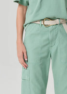 Person wearing a light green outfit with a belt on a plain background