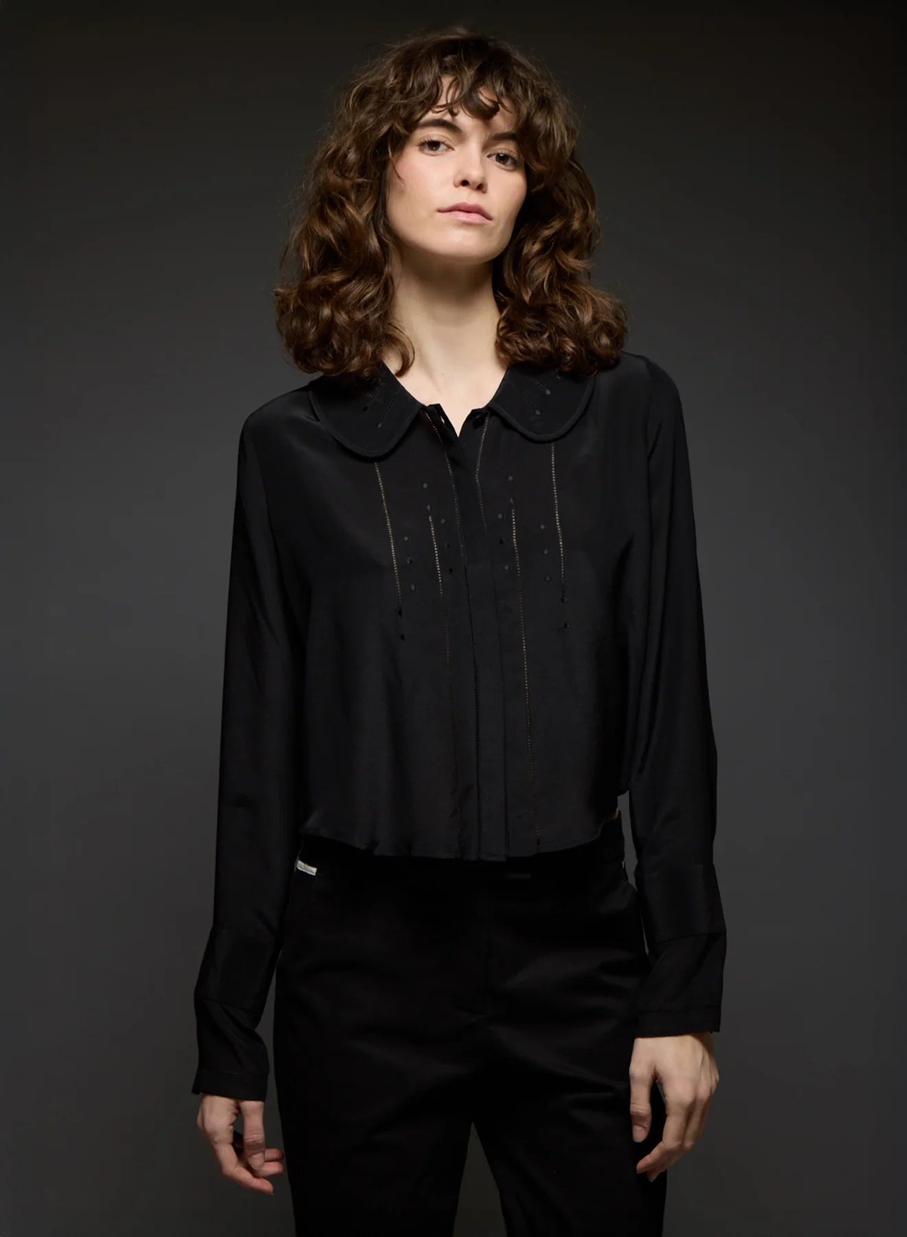 Person wearing a black blouse with a collar against a dark background
