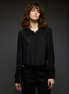 Person wearing a black blouse with a collar against a dark background