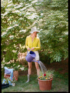 Woman watering plants in a garden with trees and flowers in the background