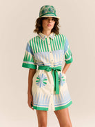 Woman wearing a colorful dress with a belt and matching hat on a plain background