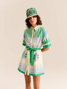 Person wearing a green and white striped outfit with a matching hat on a beige background

