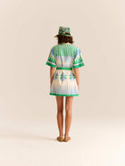 Woman wearing a green and white striped dress with a matching hat on a beige background