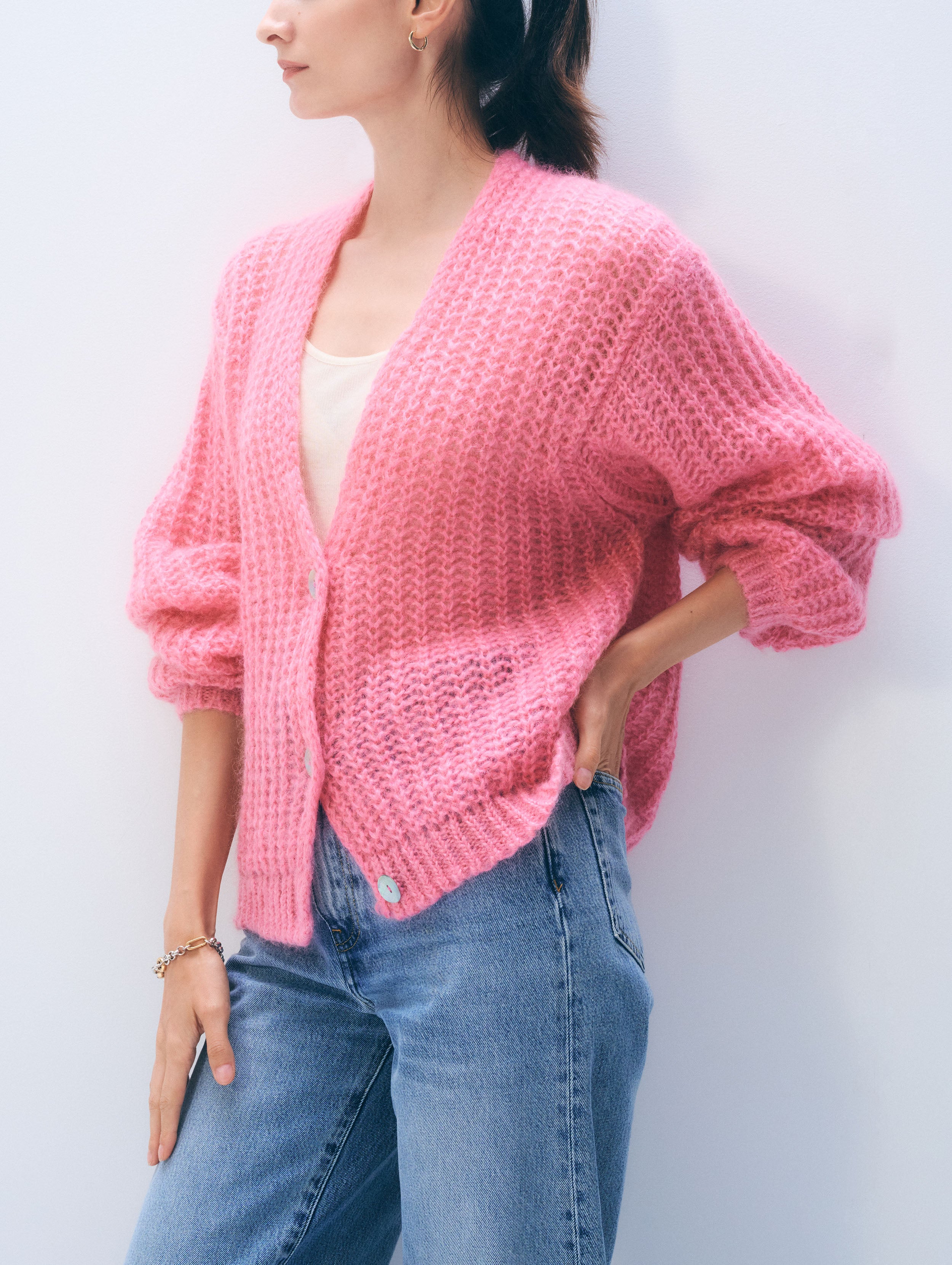 Person wearing a pink knitted cardigan and blue jeans against a white background