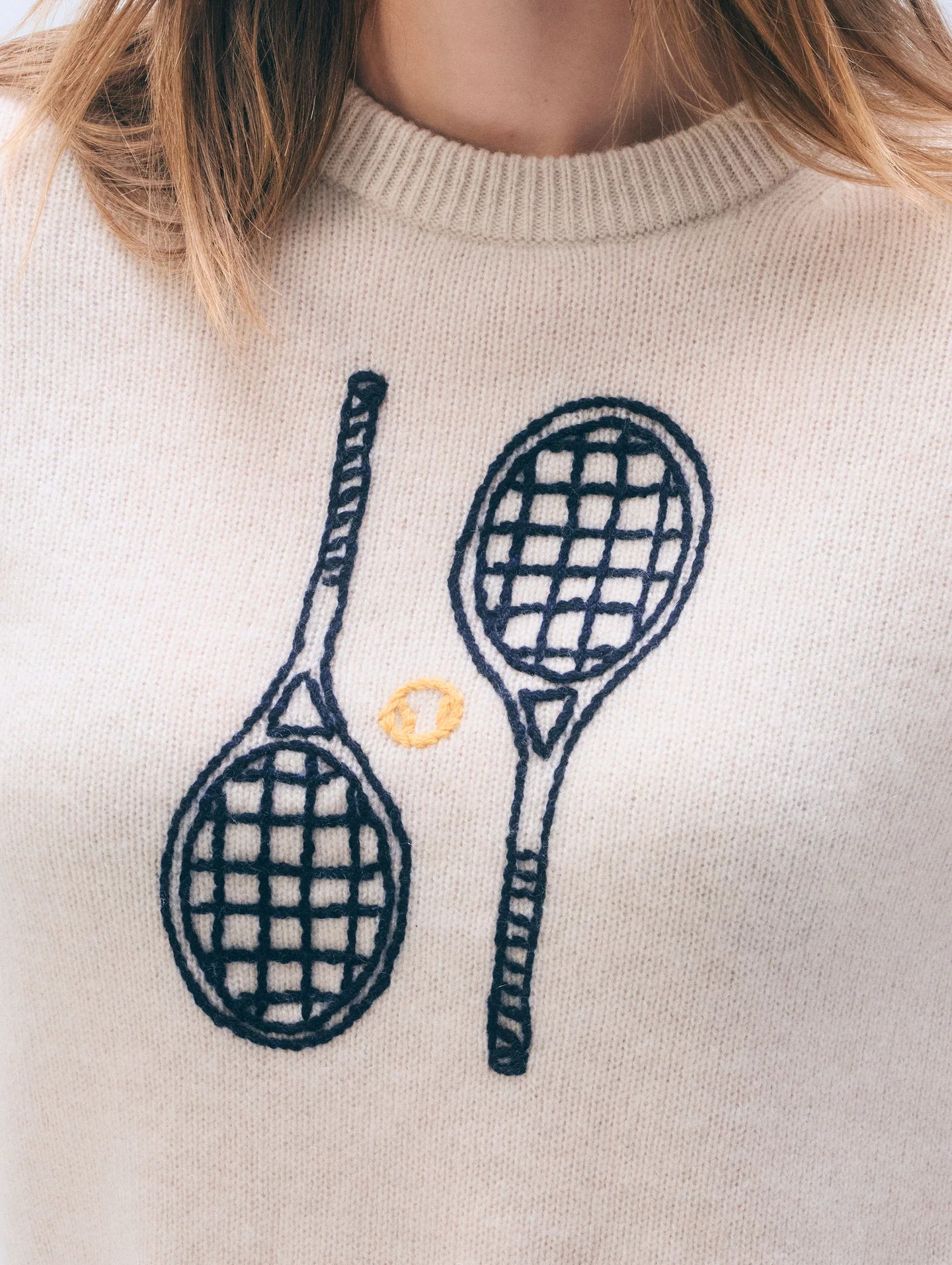 Close-up of a sweater with embroidered tennis rackets.