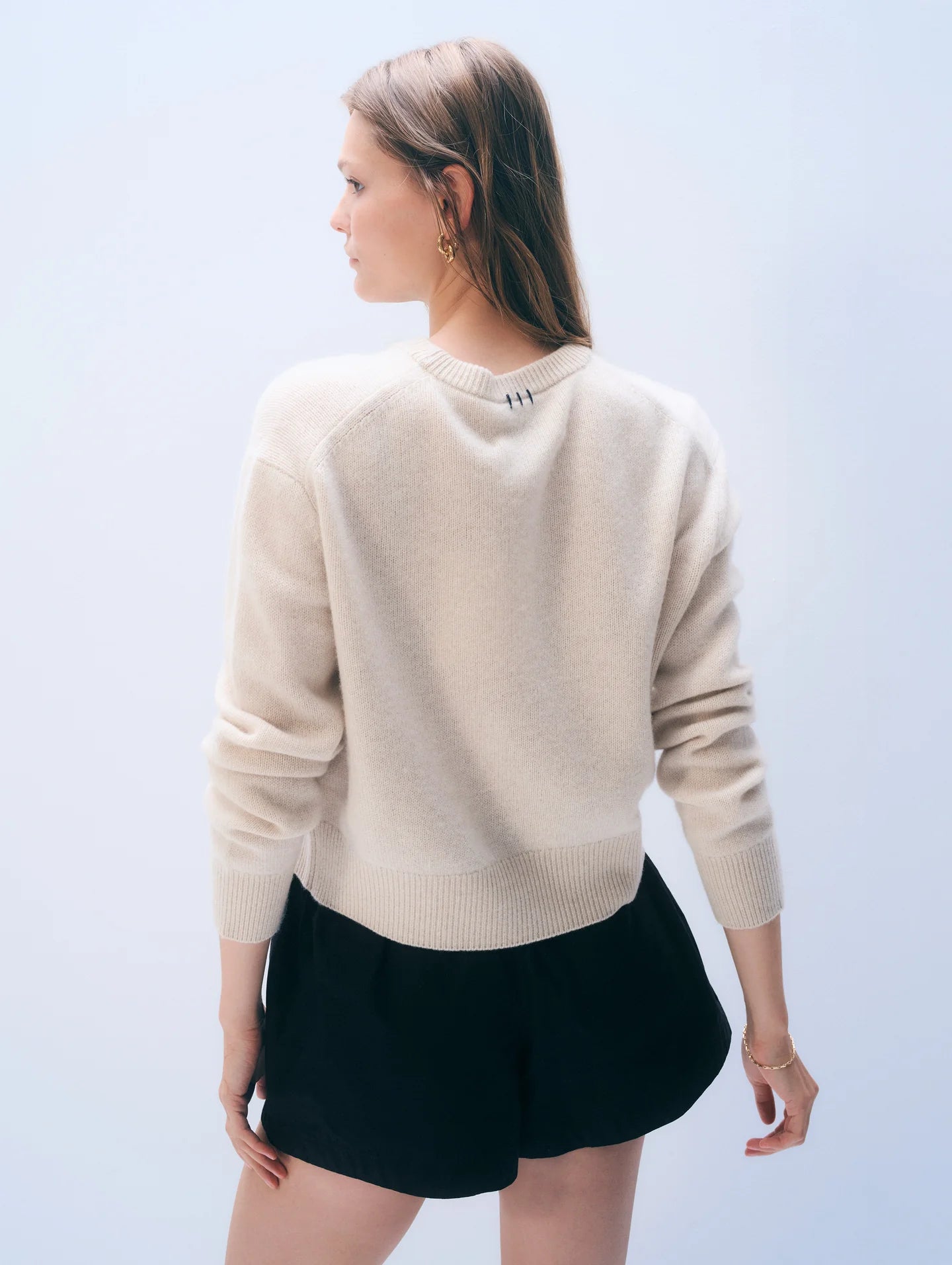 Person wearing a beige sweater and black shorts on a light blue background