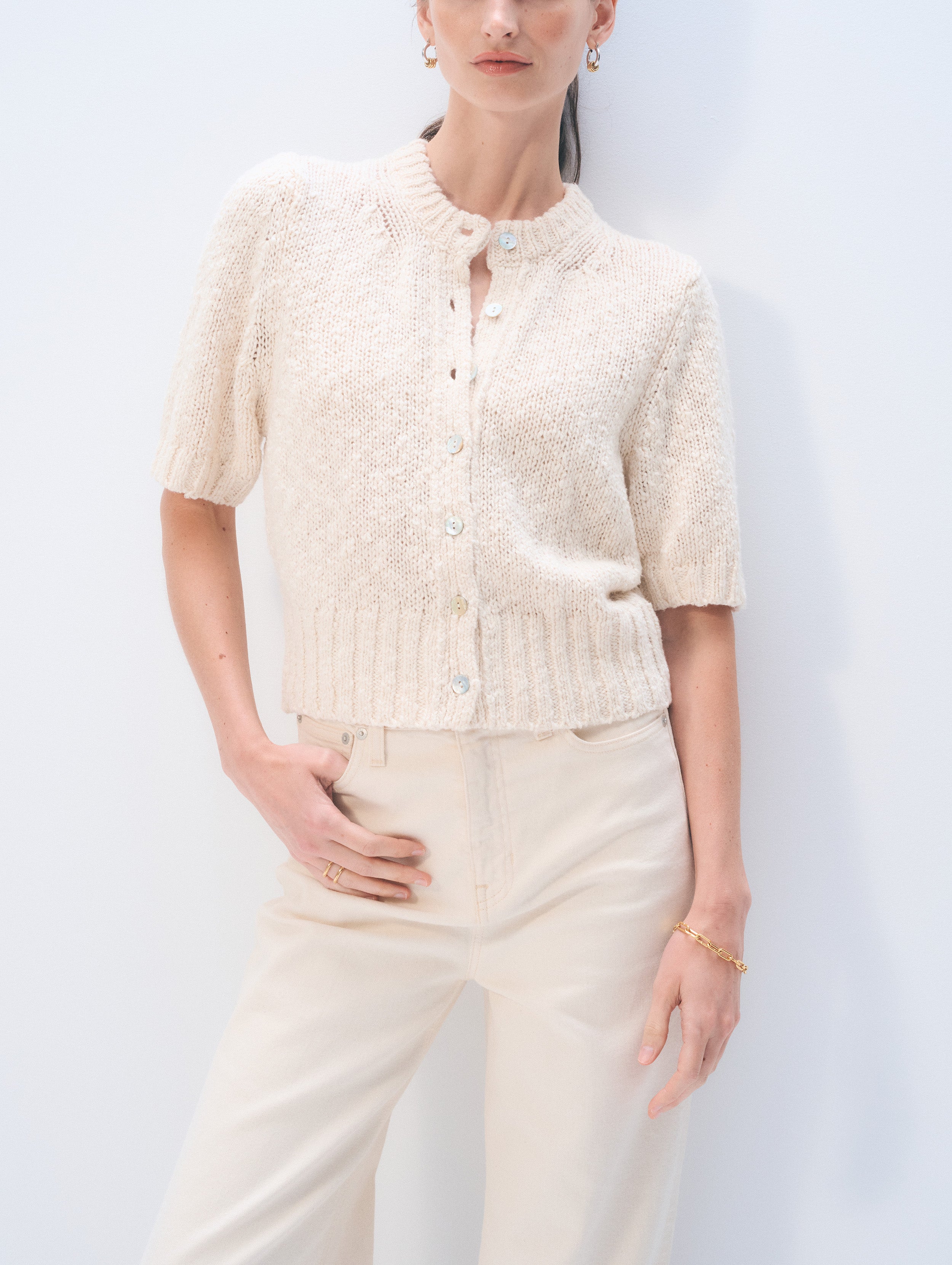 Woman wearing a cream-colored knit cardigan and pants against a white background