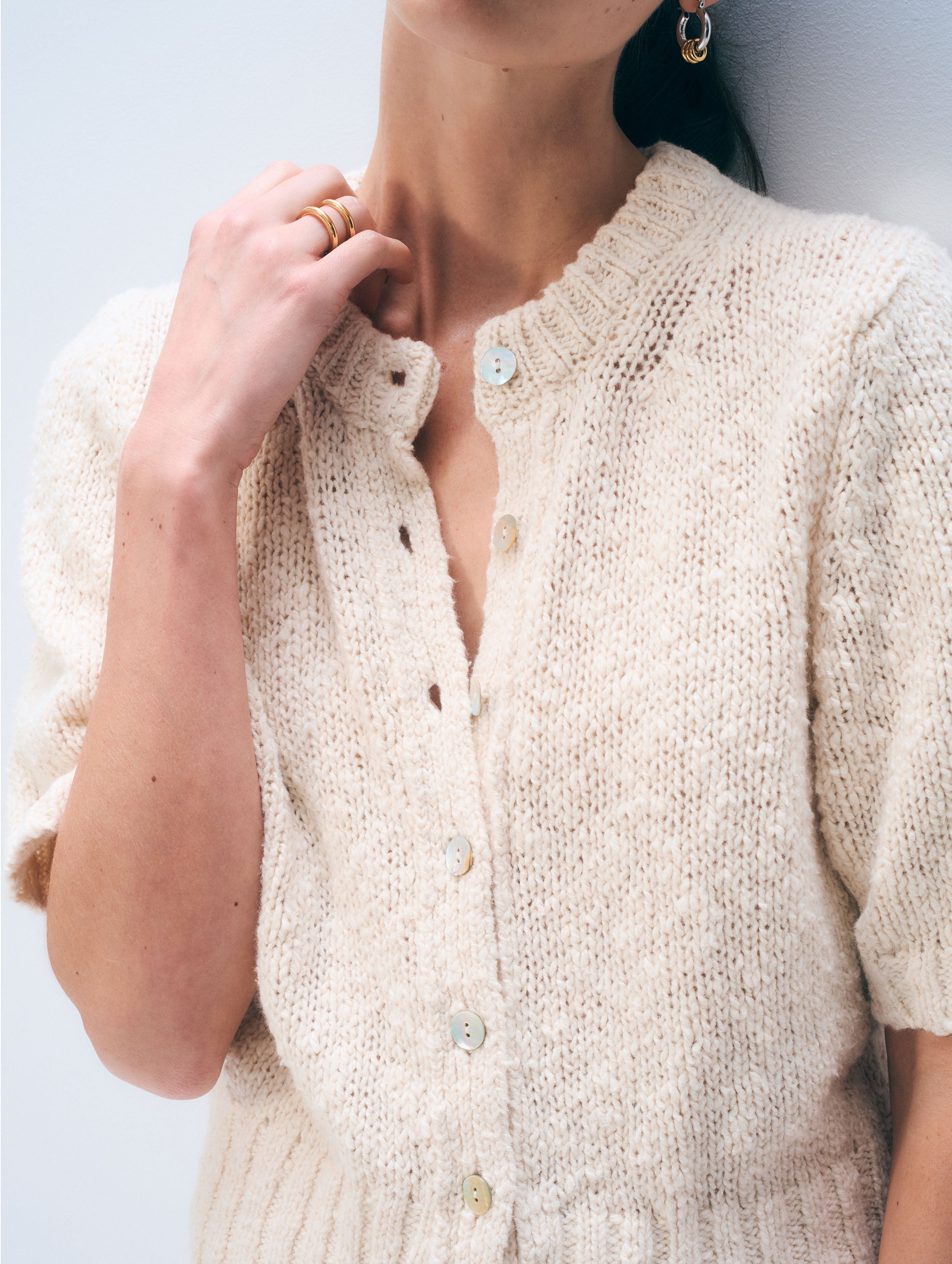 Close-up of a person wearing a beige knitted cardigan on a light background