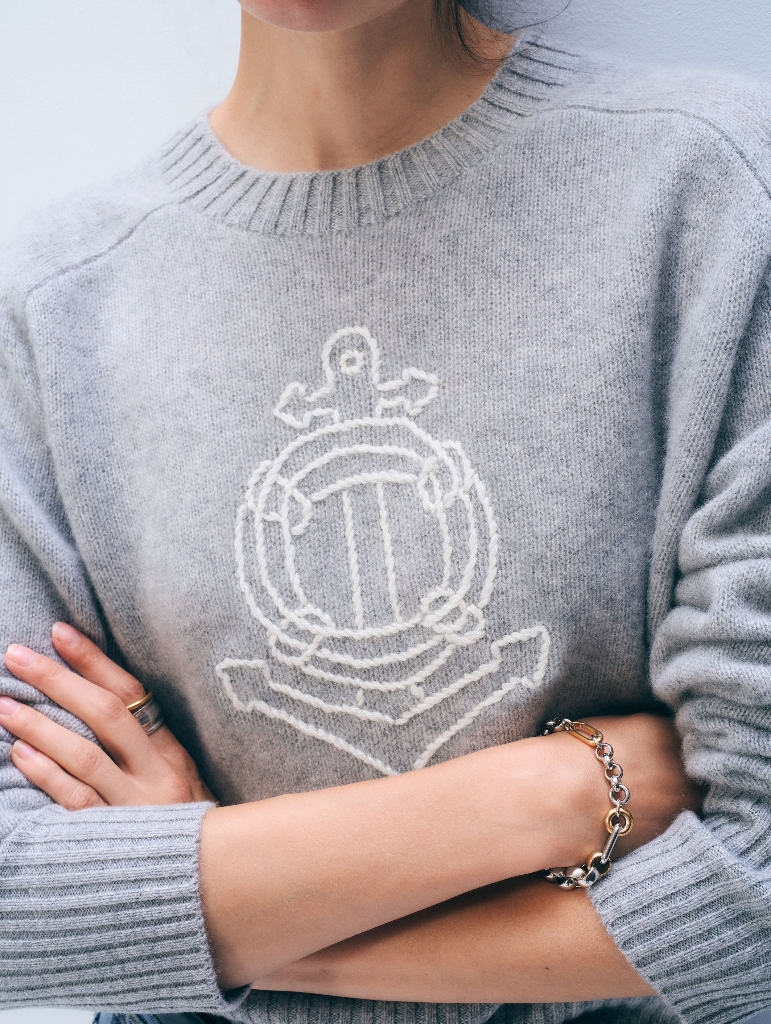 Person wearing a gray sweater with a white emblem design.