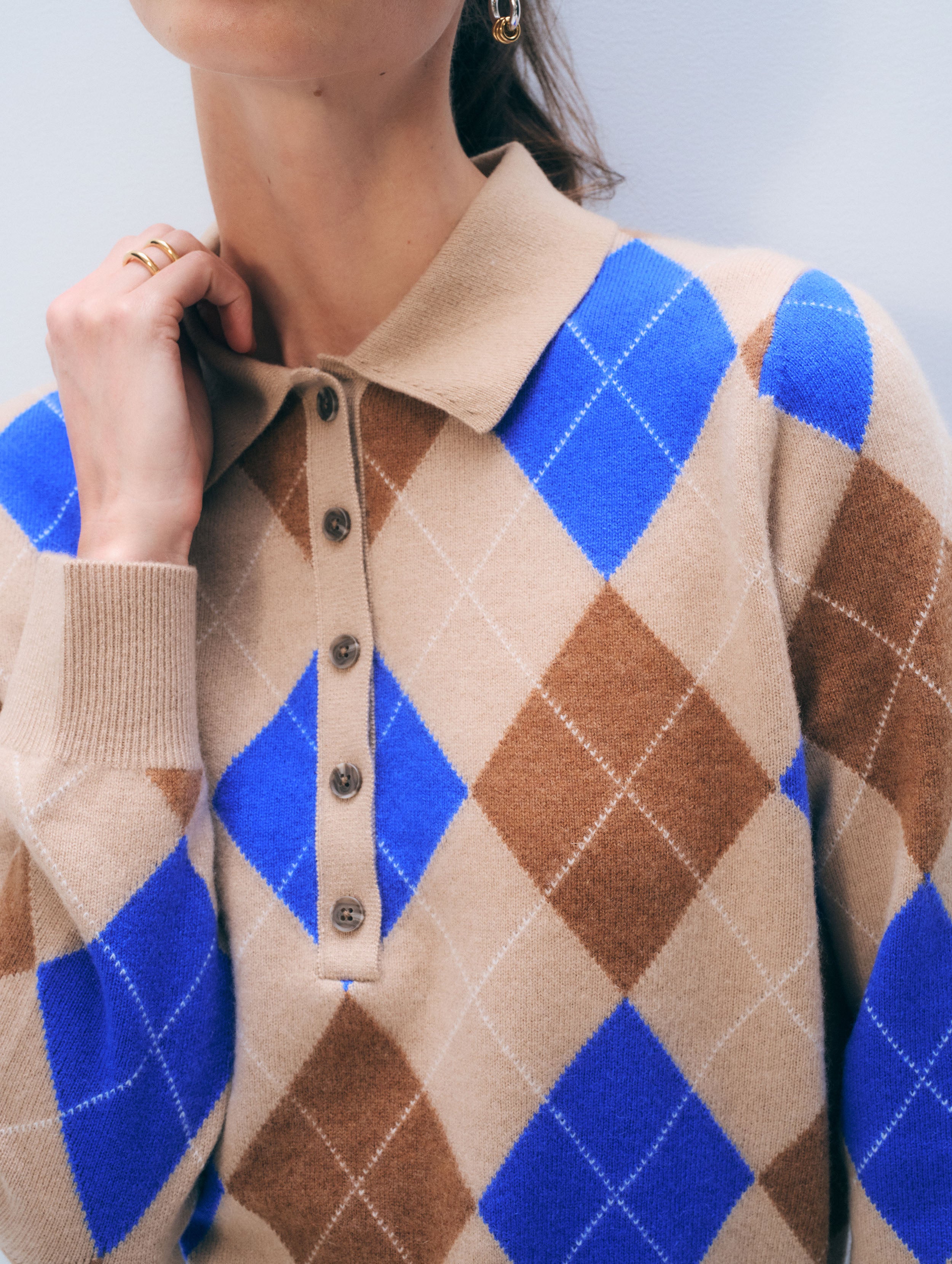 Person wearing a beige and blue argyle patterned sweater against a light gray background