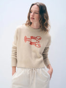 Woman wearing a beige sweater with a red lobster design on a light gray background