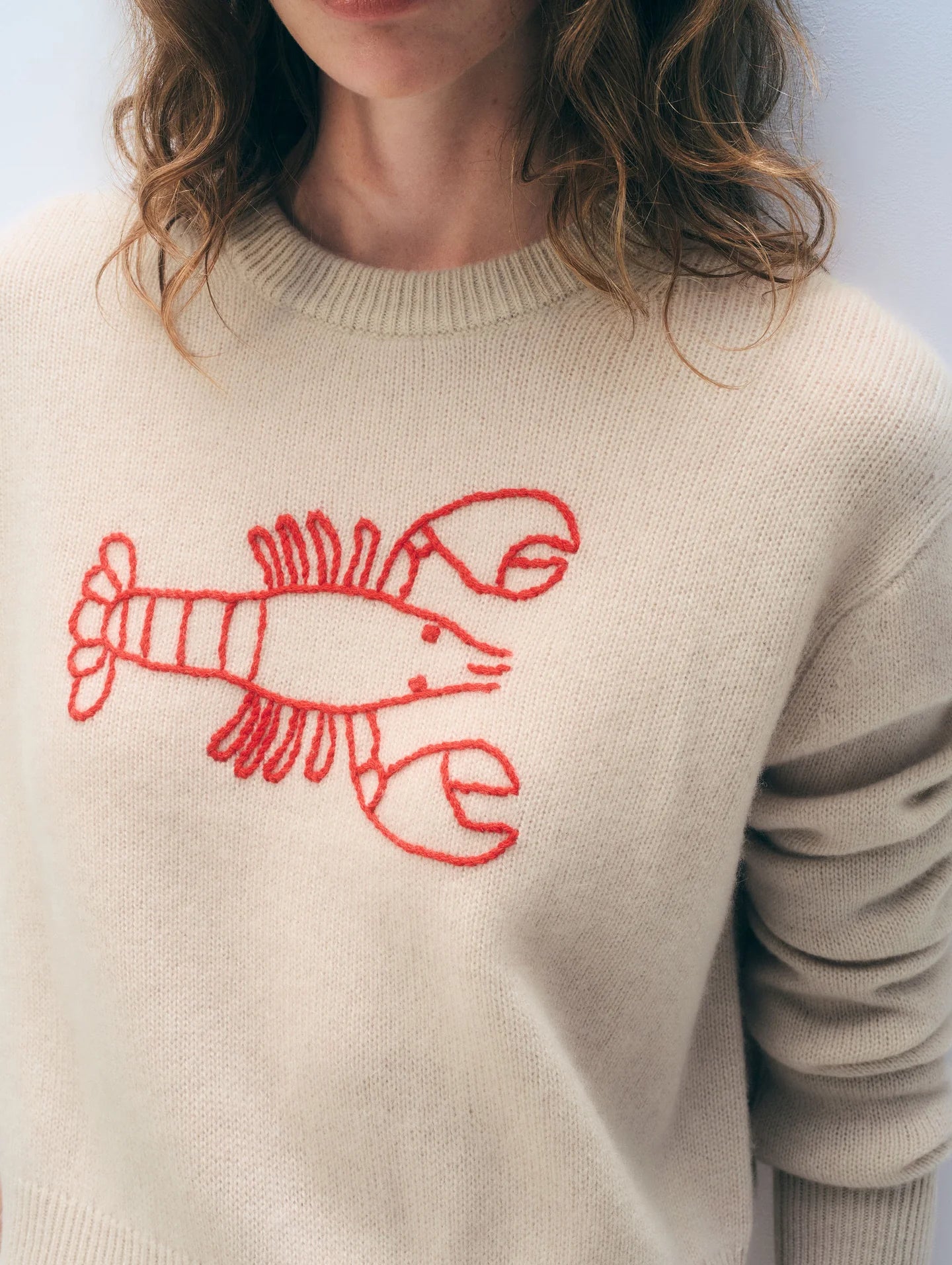 Woman wearing a beige sweater with a red lobster design on a light gray background