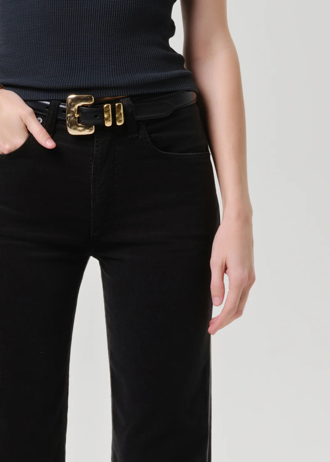 Person wearing black pants with a gold belt buckle on a plain background