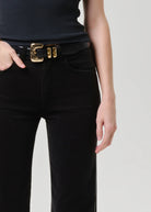 Person wearing black pants with a gold belt buckle on a plain background