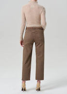 A model shown from the back wearing brown wide-leg cropped jeans, a beige mock-neck knit sweater, and beige high-heeled shoes against a light gray studio background.