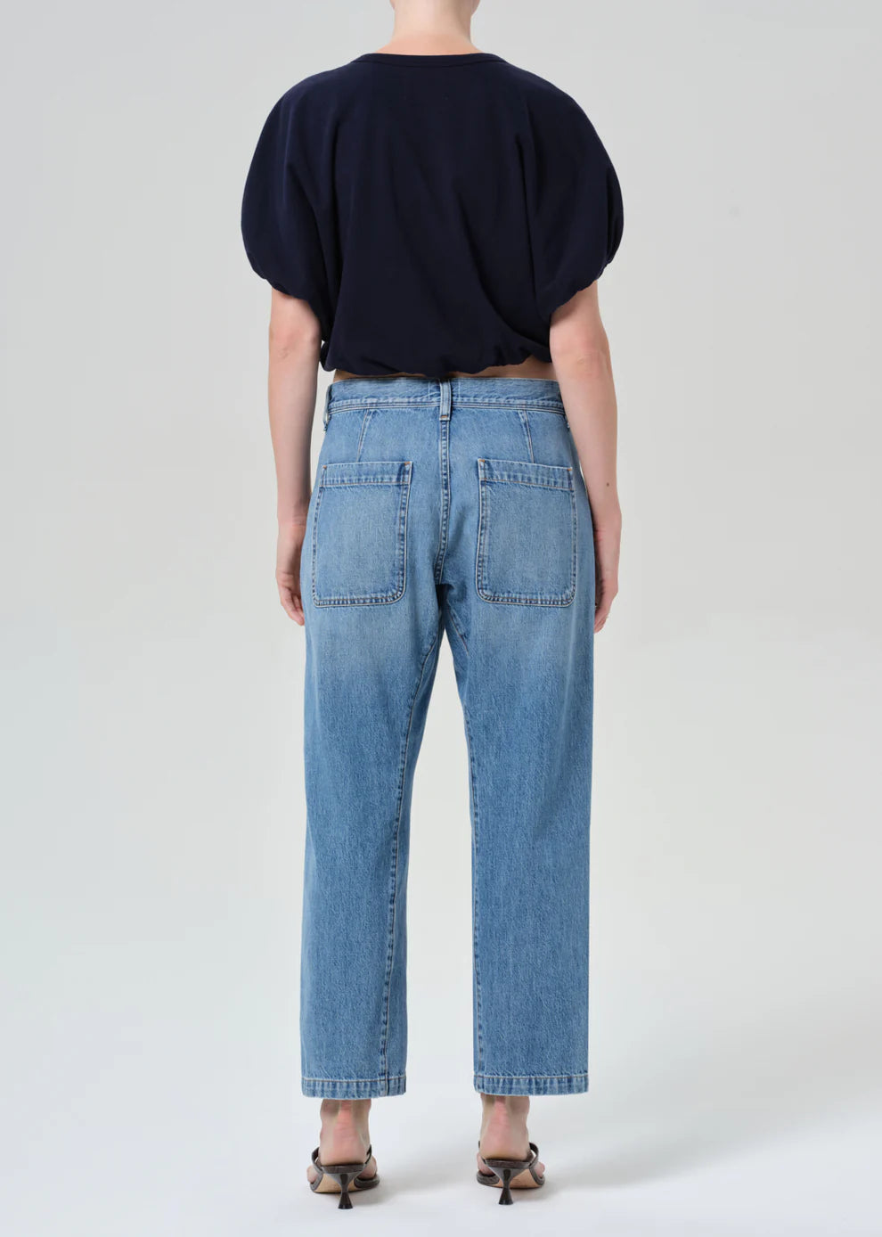 Person wearing blue jeans and a dark top on a white background