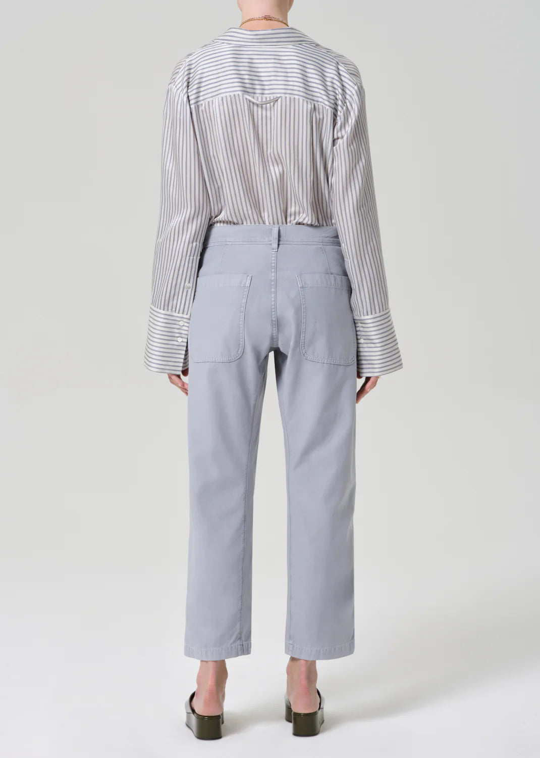 Person wearing a striped shirt and light gray pants on a white background
