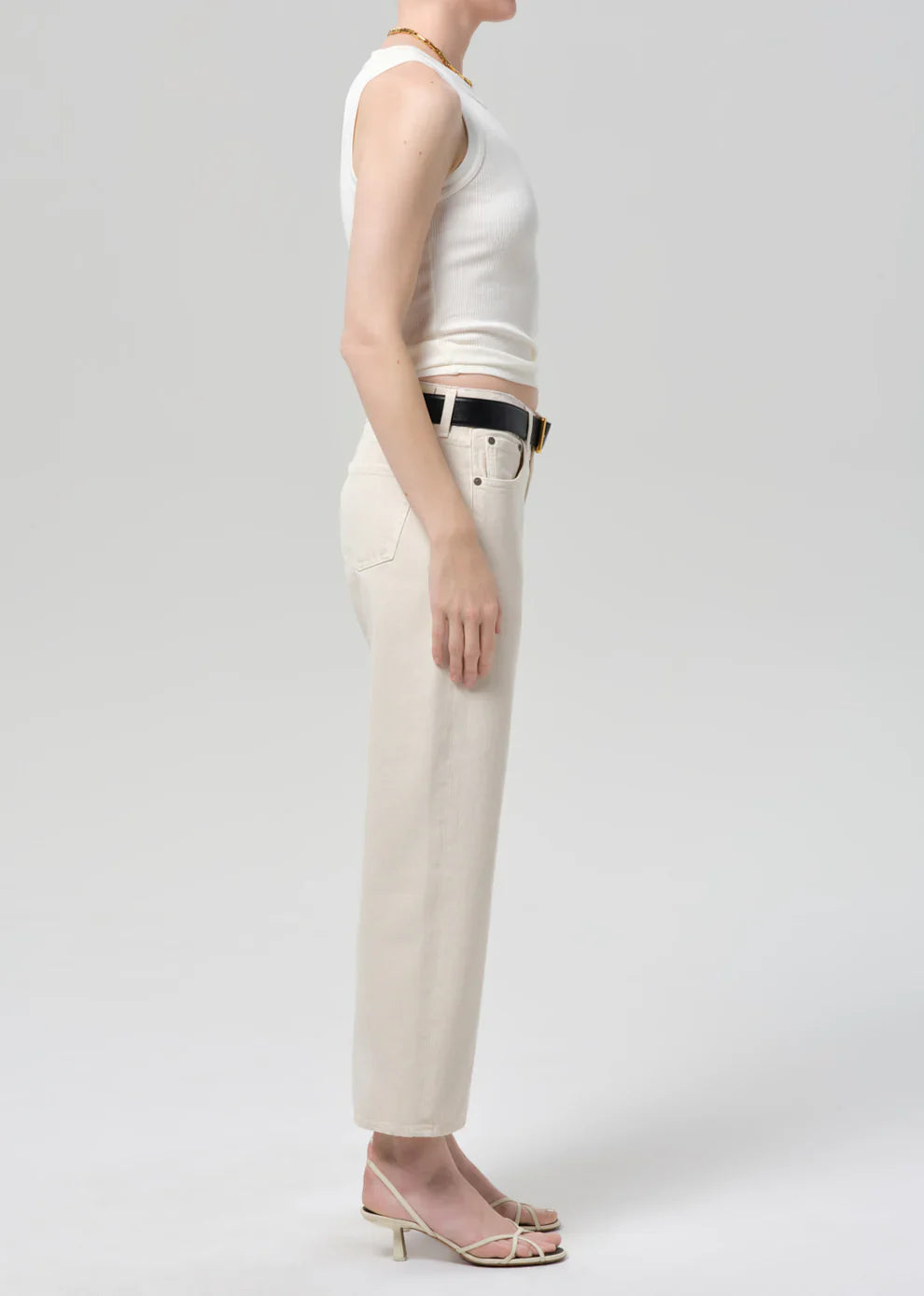 Person wearing a white sleeveless top and beige pants on a plain background