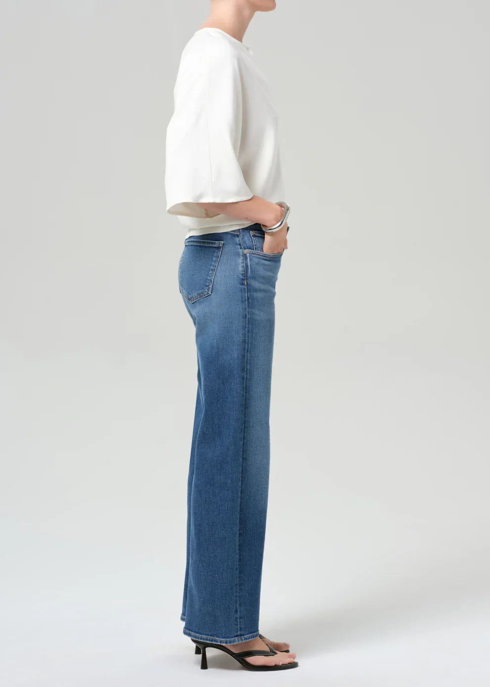 Person wearing blue jeans and a white top on a plain background