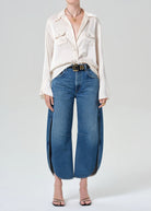 Person wearing a white blouse and blue jeans on a plain background