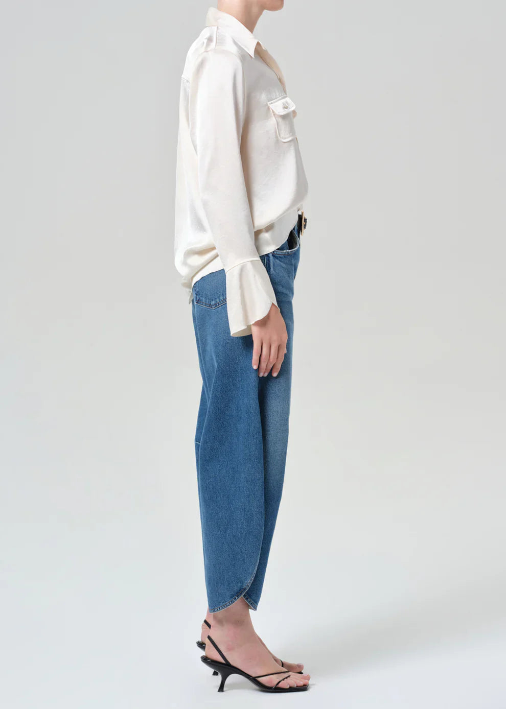 Person wearing a white blouse and blue jeans on a plain background