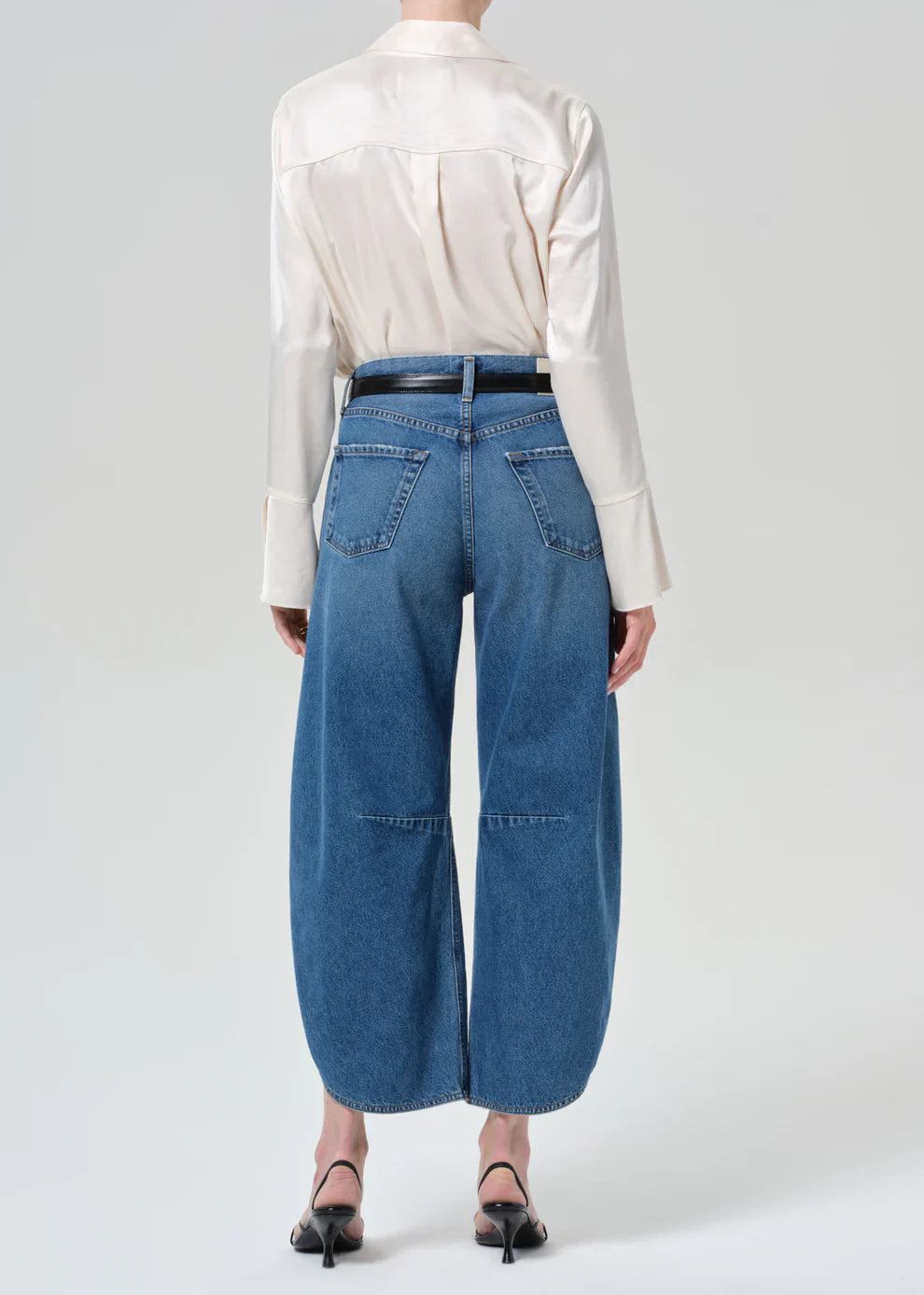 Person wearing a white shirt and blue jeans on a plain background