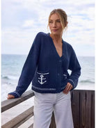 Woman wearing a navy blue cardigan with an anchor design by the ocean.