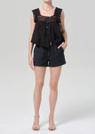Person wearing a black sleeveless top with lace details and black shorts on a white background