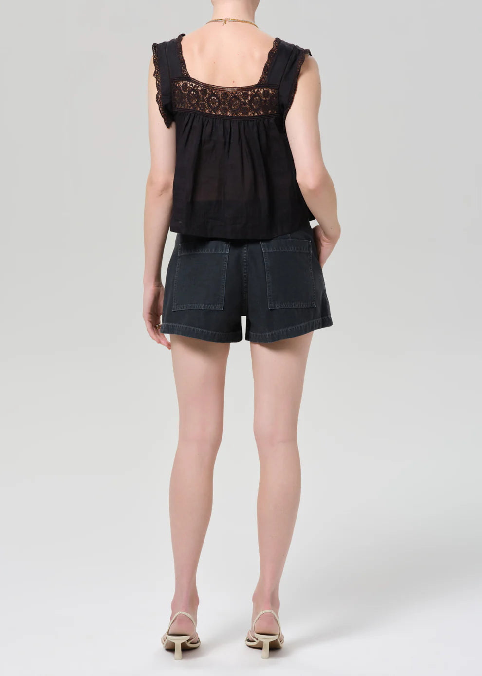 Person wearing a black sleeveless top with lace details and dark shorts on a white background