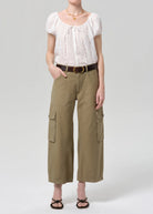 Person wearing a white blouse and beige cargo pants on a plain background