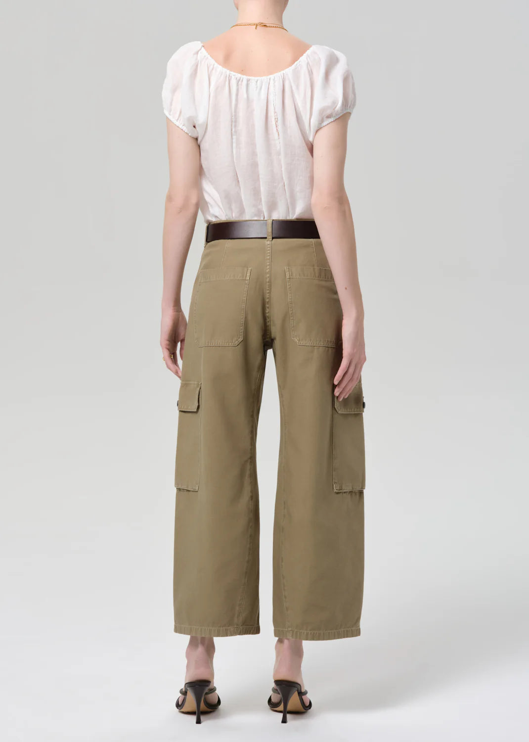 Person wearing a white blouse and green cargo pants on a plain background