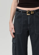 Person wearing black cargo pants with a gold belt buckle on a light gray background