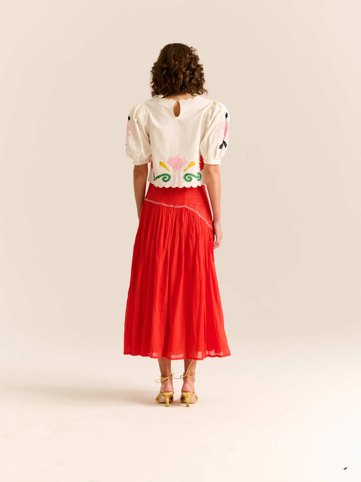 Woman wearing a white blouse with colorful patterns and a red skirt on a beige background