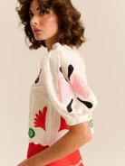 Woman wearing a white blouse with colorful floral patterns on a beige background