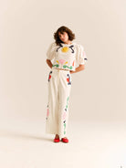 Woman wearing a white outfit with colorful floral patterns on a plain background