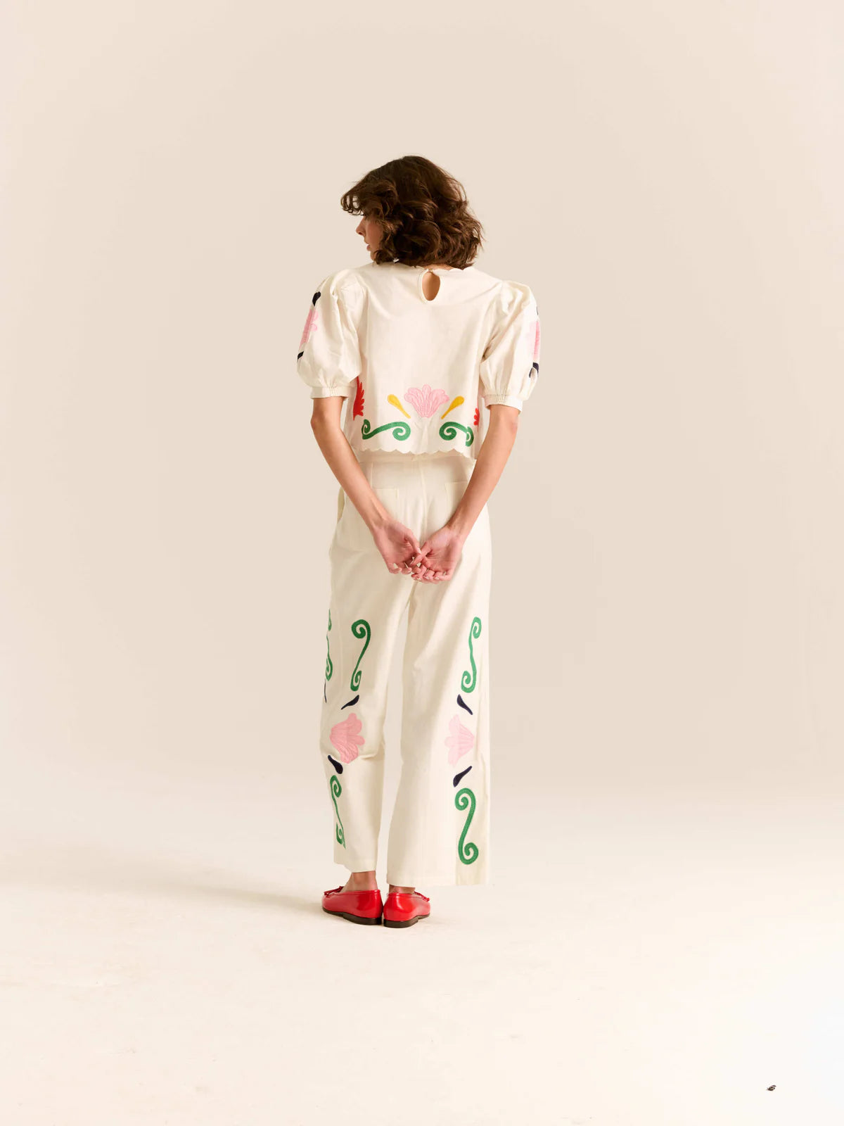 Person wearing a white outfit with colorful patterns on a plain background