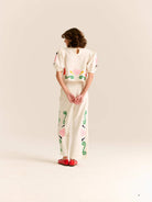 Person wearing a white outfit with colorful patterns on a plain background