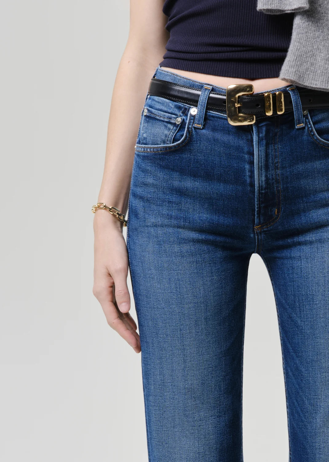 Person wearing blue jeans with a black belt on a light gray background