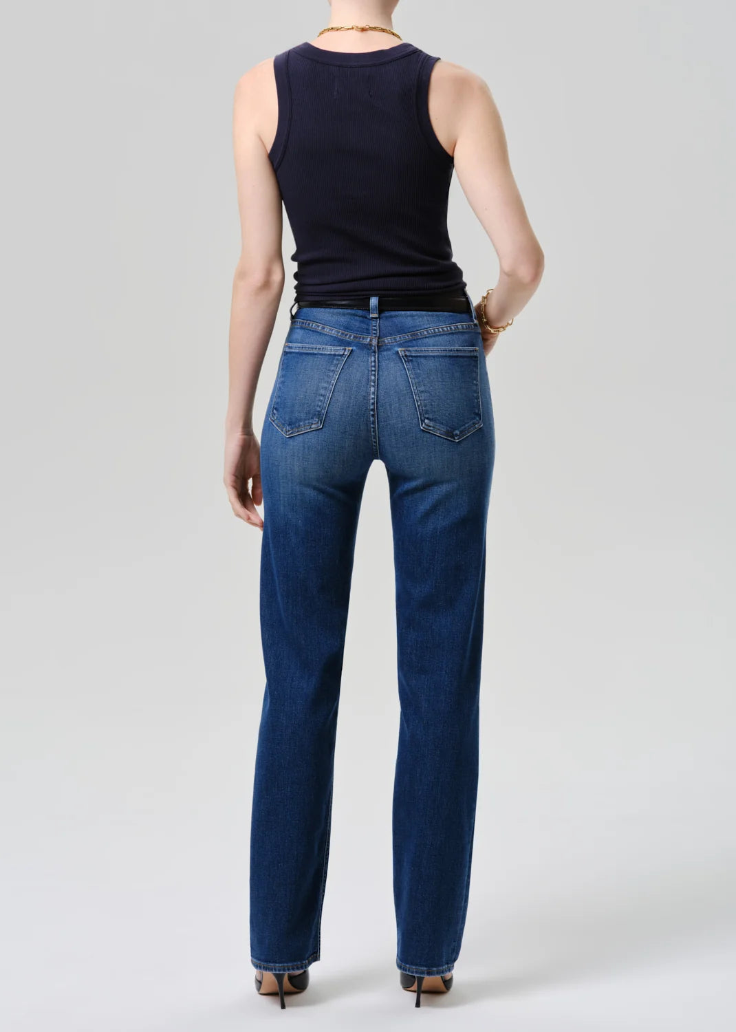 Person wearing blue jeans and a black sleeveless top on a white background