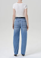 A model shown from the back wearing light-wash blue wide-leg jeans, a white short-sleeve t-shirt, and black heels against a plain light gray studio background.