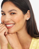 A close-up of a smiling woman with dark hair wearing a small curved row of sparkling stud earrings against a clean white background.