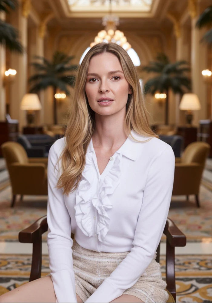 Woman in a white blouse sitting in a luxurious room with ornate decor.