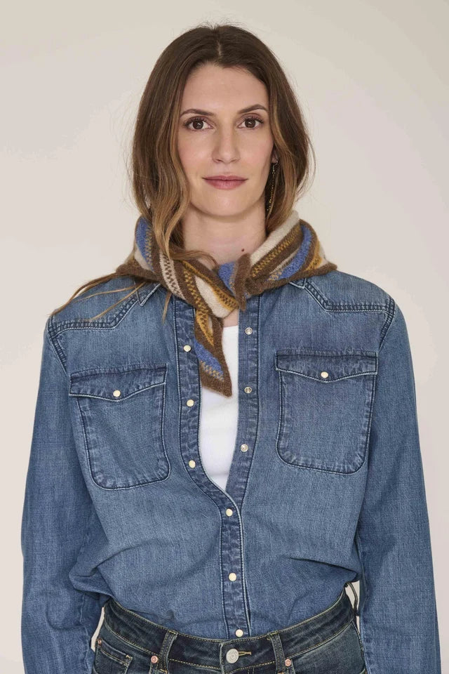 A woman wearing a blue denim western-style shirt jacket over a white top, styled with a patterned brown and beige scarf, against a plain beige background.