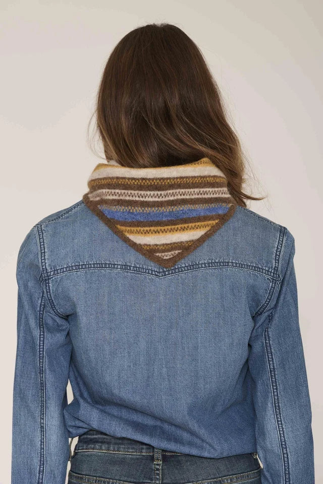 A woman viewed from behind wearing a blue denim jacket over a striped knit cowl neck scarf in brown, beige, and blue tones.