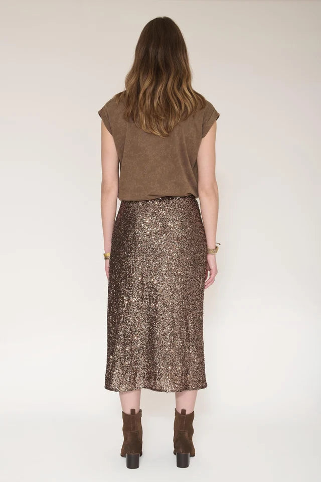 A woman shown from the back wearing a brown sleeveless top and a shimmering bronze sequined midi skirt, paired with brown ankle boots, against a plain light background.
